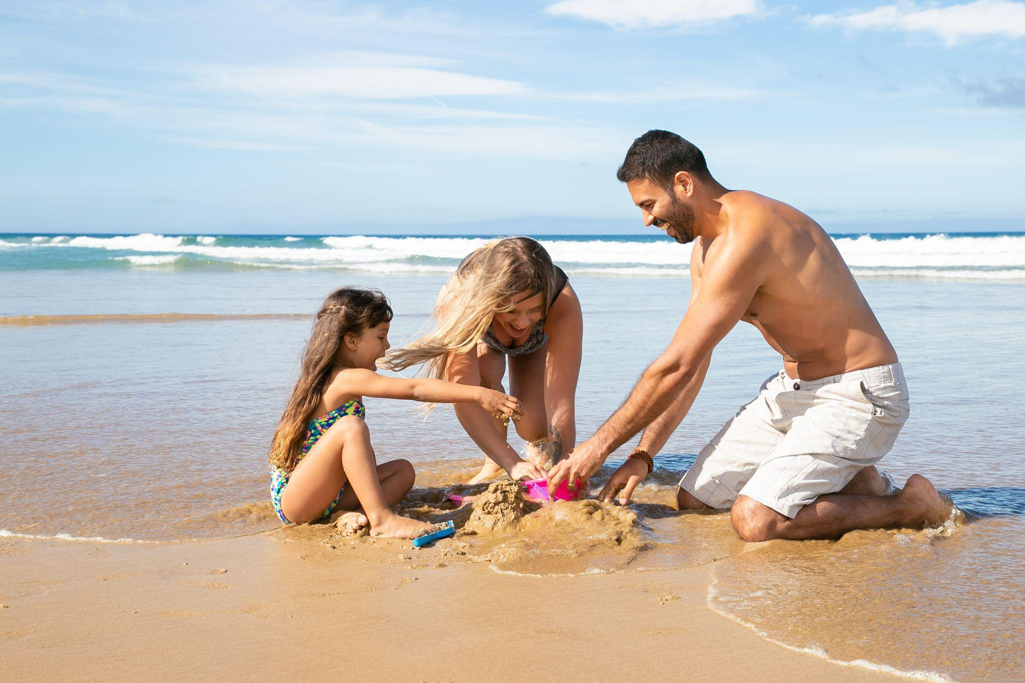 Smiling parents and daughter building a sandcastle at the beach.